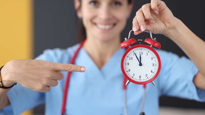 A healthcare worker is holding and pointing at a red clock