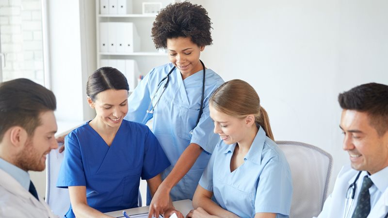 Five healthcare workers are gathered around a table smiling and talking.